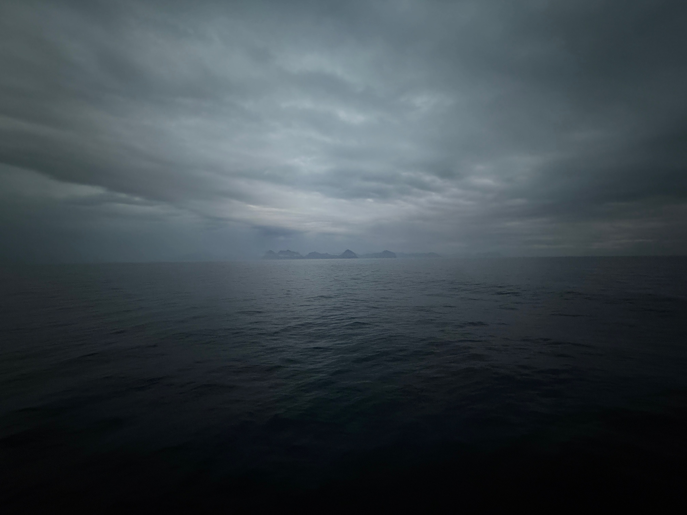 Mørkt, stille hav under tunge skyer, med fjell langt ute i horisonten.